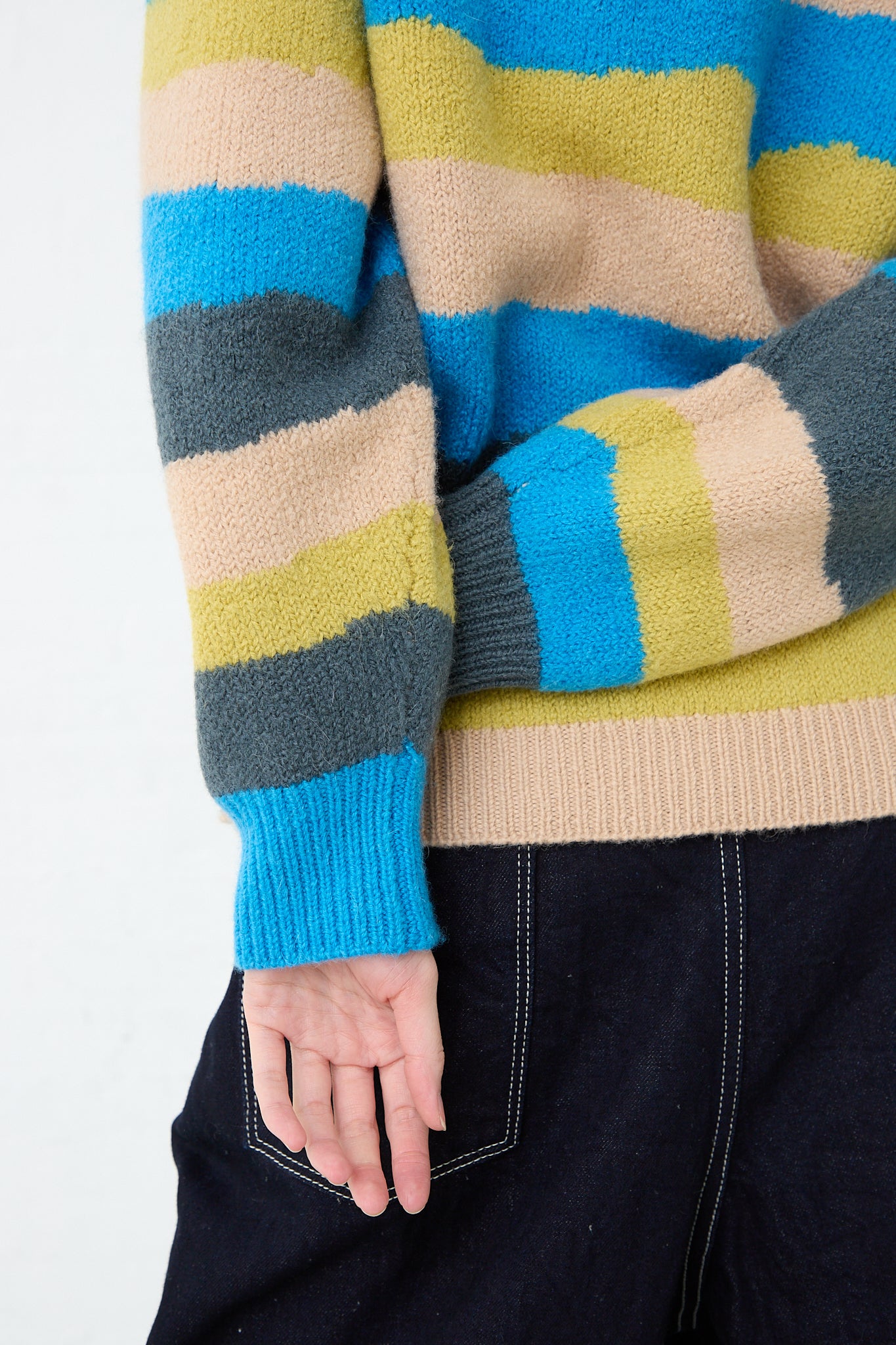 A woman wearing a Light Wind Sweater in Blue Mix by Mina Perhonen featuring a stripe design in blue, green, and yellow. Back view and up close showcasing sleeves.