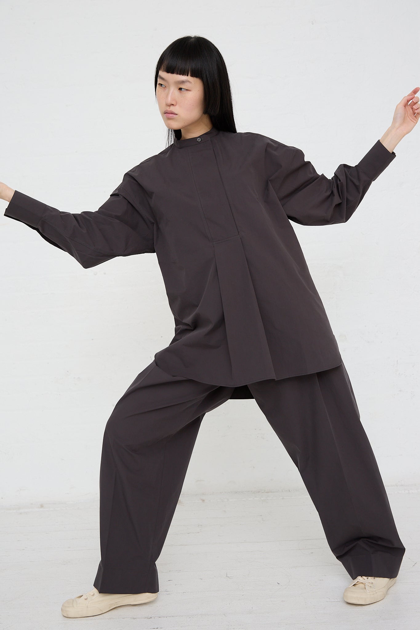 A woman is wearing a long-sleeved Frink Half Placket Shirt in Asphalt by Studio Nicholson.