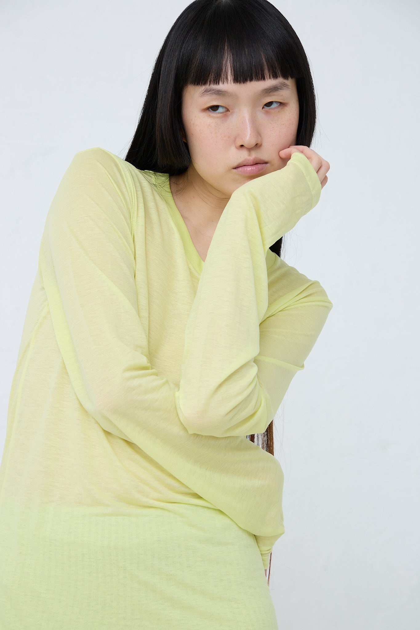 Bamboo Long Sleeve Tee in Lime, made by Baserange, is crafted from sustainable bamboo lyocell. Front view. Model's arms are crossed and the left hand is placed under her chin.