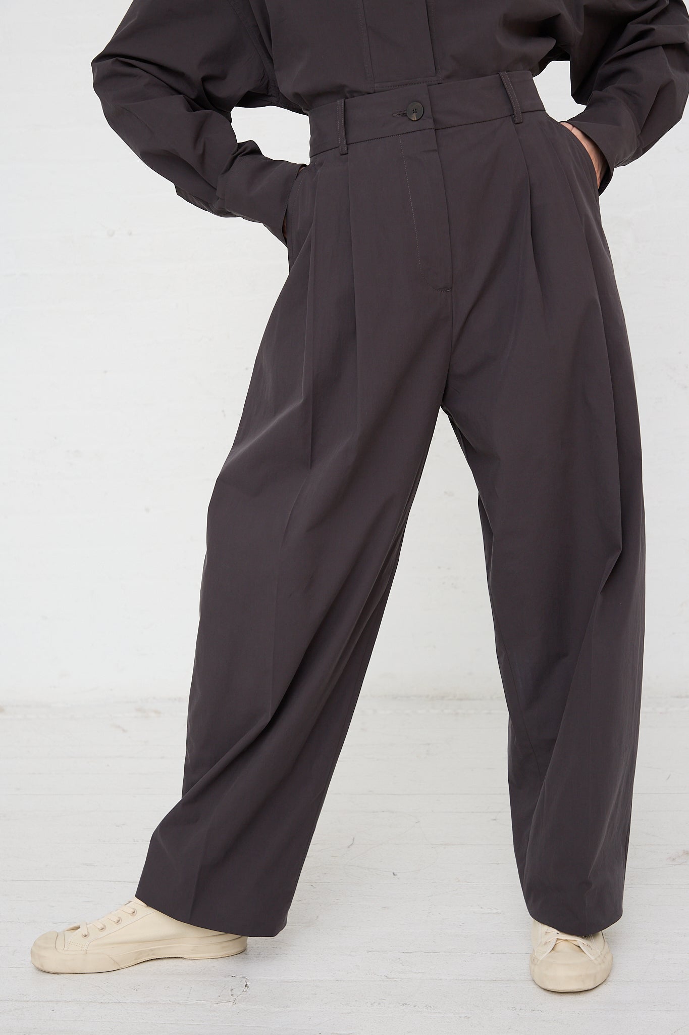 A model wearing an Acuna Double Pleat Front Trouser in Asphalt by Studio Nicholson and a white shirt. Front view of pants. Up close.