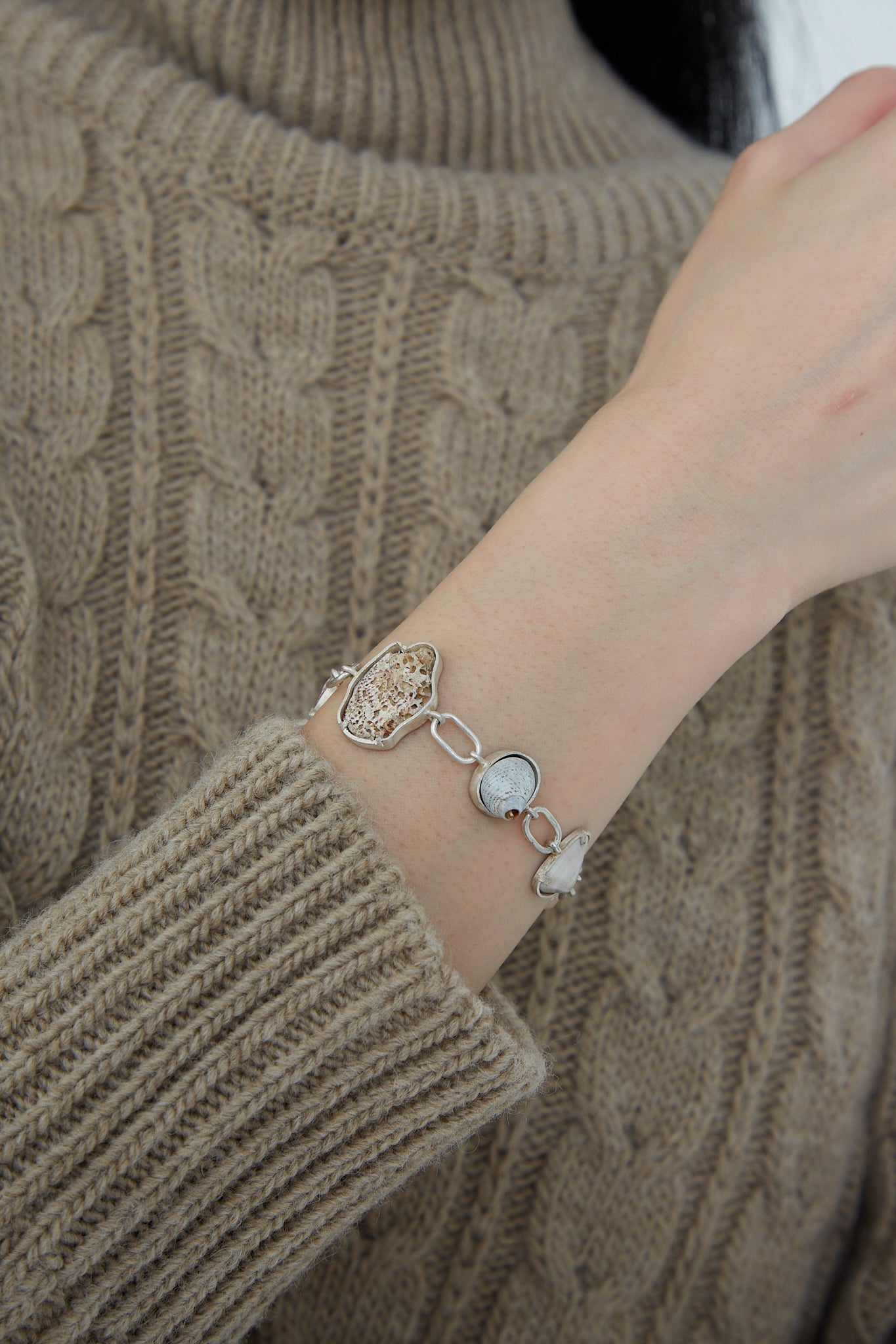A woman donning a one-of-a-kind sweater, accentuated by a La Ma r Sterling Silver Bracelet 001 A, carefully exhibits her found shells collection.