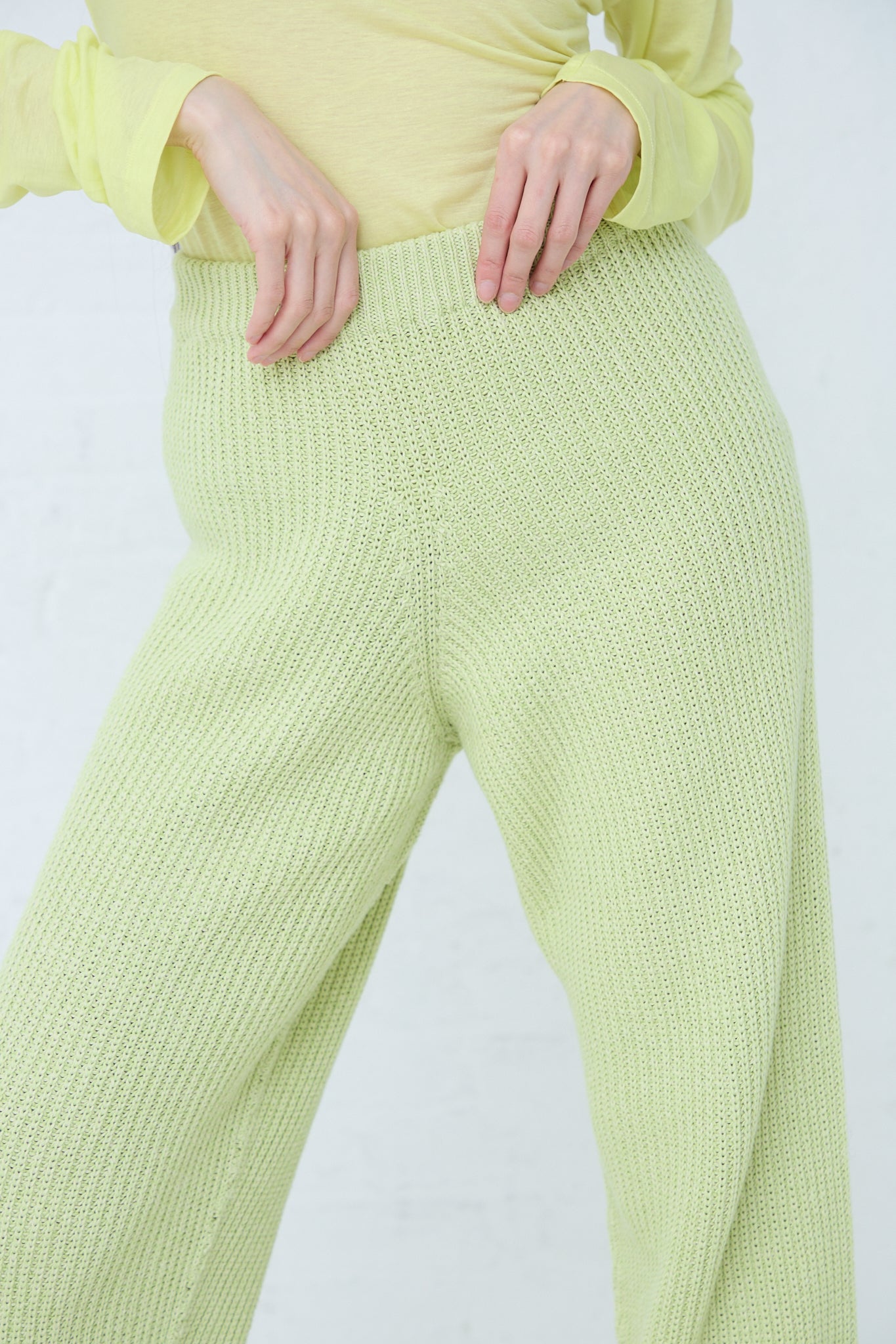 A woman wearing Baserange's sustainably produced Cotton Dodd Pant in Mimosa, a lime green ribbed pant with an elasticated waist, and a yellow top made from organic cotton.