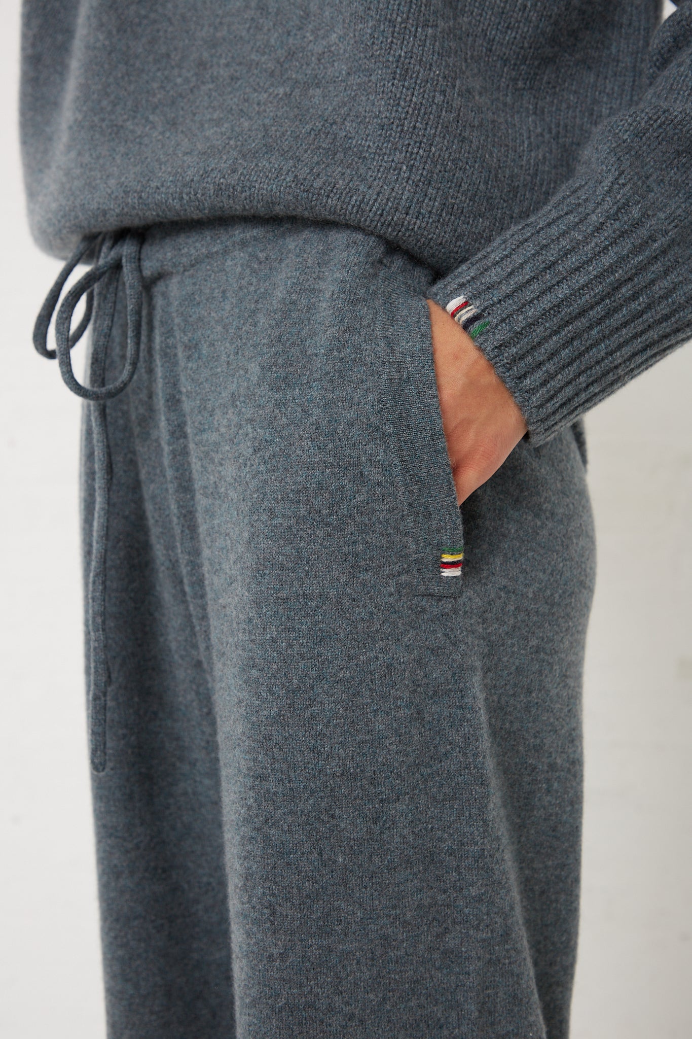 A man wearing a grey sweater and Extreme Cashmere's No. 320 Rush Trouser in Wave.