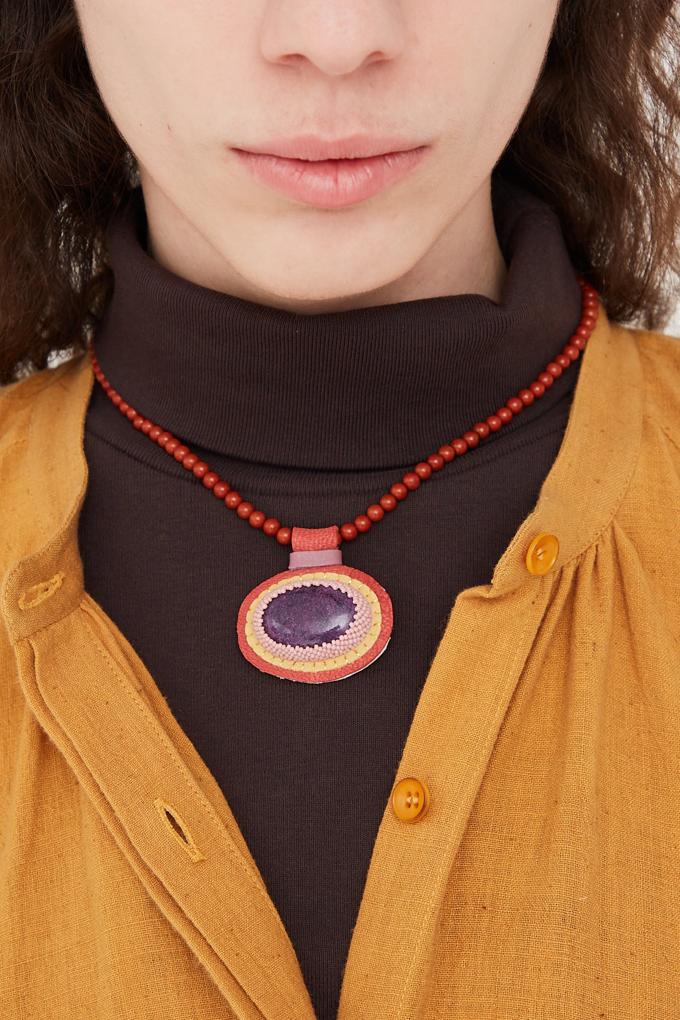 A woman wearing a Robin Mollicone Charm Necklace in Red Jasper Beads and Purpurite Charm, adorned with purpurite charm.