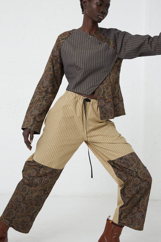 A woman in a brown and tan outfit, wearing an adjustable waist belt, is standing confidently in front of a white wall, wearing the SC103 Check Cotton Domain Pant in Tent.