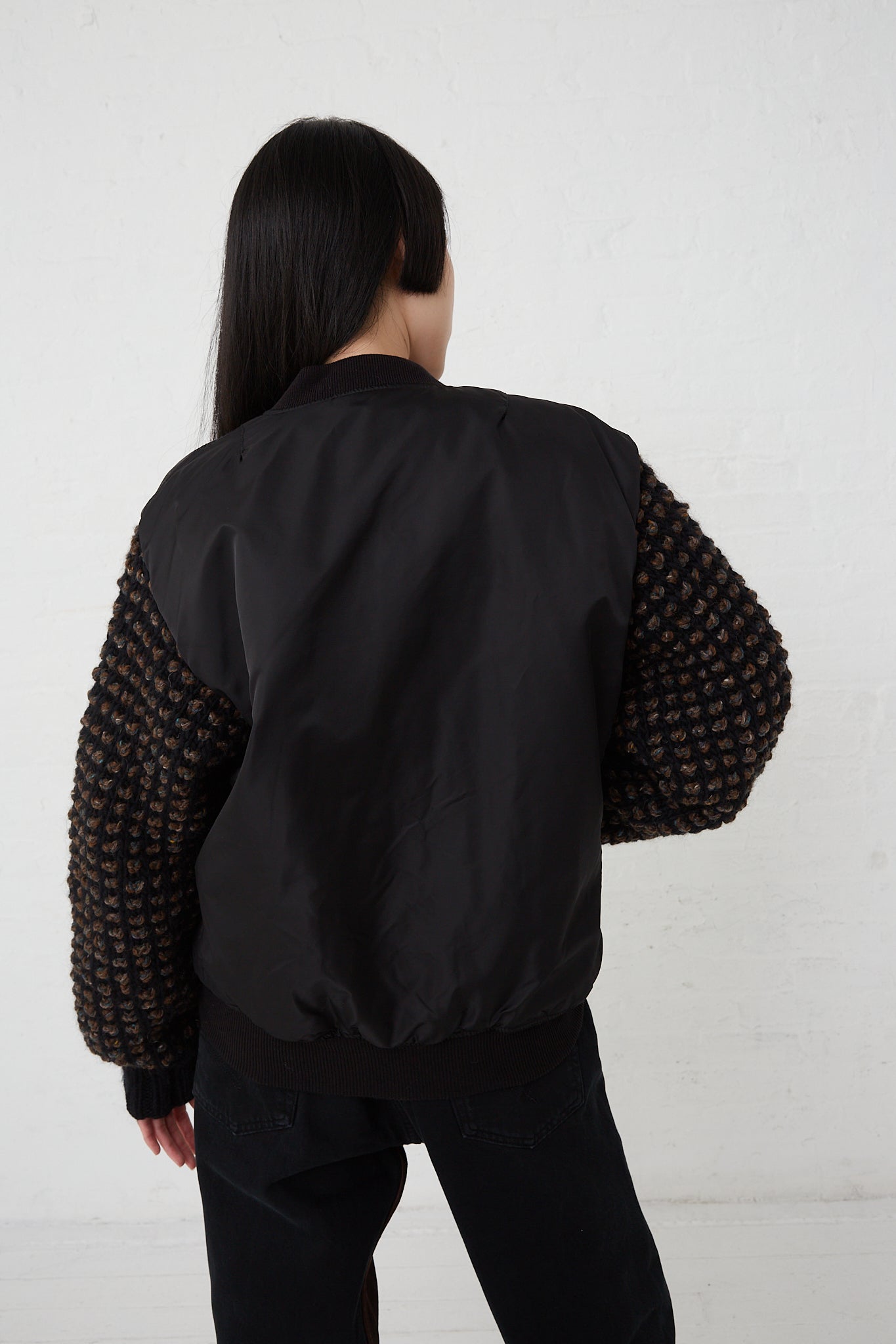 A woman showcasing the Bless Sleeve Bomber No. 70 in Black, an oversized fit black bomber jacket made of a nylon and wool blend.